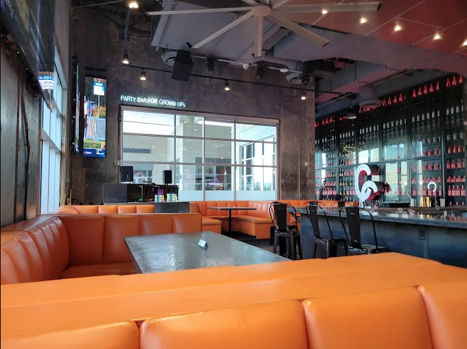 Daytime bar interior with PARTY BAR FOR GROWN UPS neon and orange leather booths