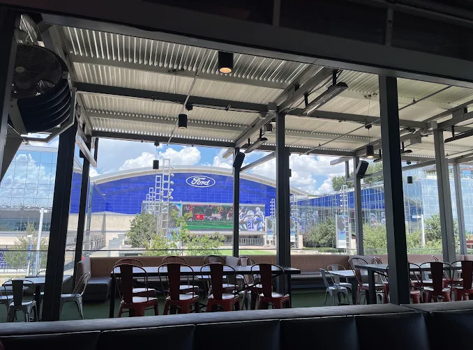 Covered daytime patio with empty tables looking across at the Ford Center at The Star