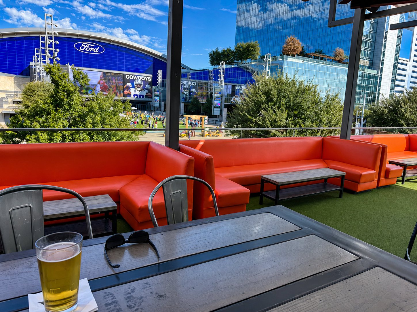 Rooftop patio with orange booths and a cold beer, looking across at the Ford Center and Cowboys screens